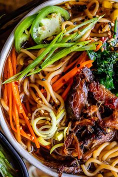 a bowl filled with noodles, meat and veggies on top of a table