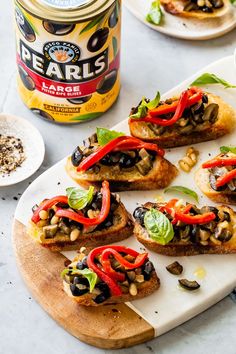 several pieces of bread with red peppers and black olives on it next to a jar of beans