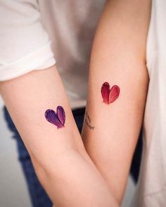 two people with matching tattoos on their arms holding each other's hands, both showing the same heart shape