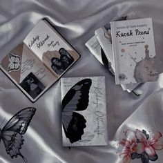 three books with butterflies on them laying on a satin bed sheet, one is open and the other two are closed