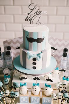 a blue and white cake sitting on top of a table next to cupcakes