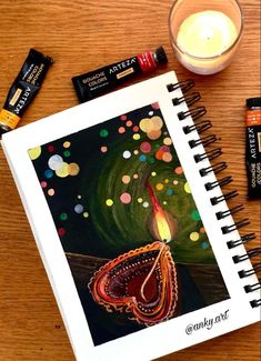 an open spiral notebook sitting on top of a wooden table next to a candle and batteries