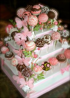 a three tiered cake decorated with pink and brown candies, chocolate lollipops, and flowers