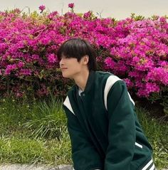 a young man sitting on the ground in front of pink flowers and grass with his hands behind his head