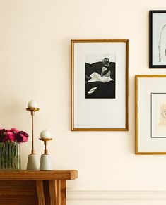 three framed pictures hang on the wall above a table with vases and flowers in front of it