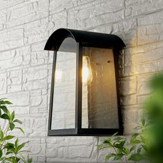 an outdoor light on the side of a white brick wall next to a potted plant