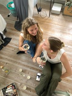 two young women sitting on the floor drinking wine and conversing with each other