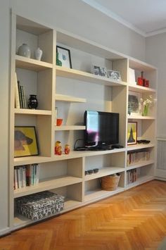 a living room filled with lots of white bookshelves next to a tv on top of a wooden floor