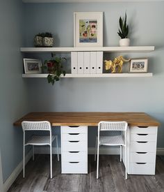 two white chairs sitting at a wooden table in front of shelves with pictures on it