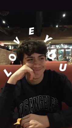 a young man sitting at a table with his hand on his chin and the words love you above him