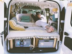 a woman laying on top of a bed in the back of a white van with its doors open