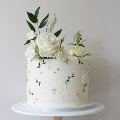 a white cake with flowers and greenery on top is sitting on a wooden stand