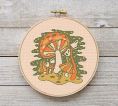 a cross - stitch pattern with an image of a mushroom in the forest on a white wooden background