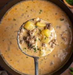 a ladle full of soup with meat and potatoes in it, ready to be eaten