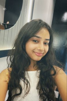 a girl with long dark hair is smiling for the camera in front of a mirror