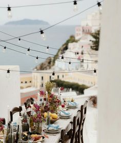 an outdoor dining table set with plates and wine glasses on it, overlooking the ocean