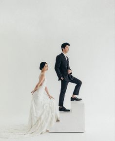 a man in a suit and woman in a wedding dress sitting on a white pedestal