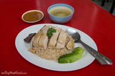 a white plate topped with rice and meat next to bowls of dipping sauces on a red table