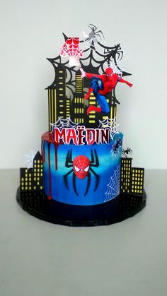 a spiderman birthday cake on a black plate with white and blue icing in the shape of a cityscape