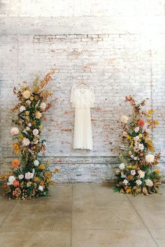 an image of a wedding dress on display in front of flowers and brick wall background