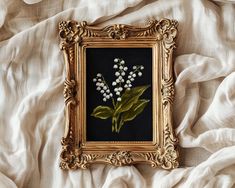 an ornate gold frame holds a bouquet of lily of the valley flowers