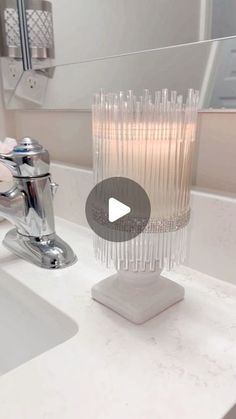 a bathroom sink with a clear glass vase on it's counter top next to a faucet