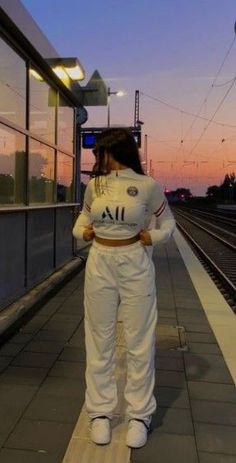 a woman in white is standing on the train tracks at sunset with her back to the camera