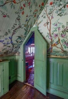 an open door in the corner of a room with floral wallpaper and green cupboards