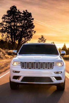 two white jeeps driving down the road at sunset