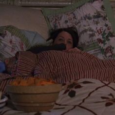 a woman laying in bed next to a bowl of food