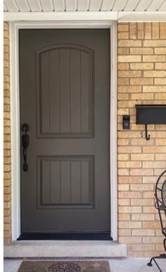 a black iron chair sitting in front of a gray door on a brick wall next to a metal planter