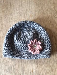 a crocheted hat with a pink flower on the front sits on a wooden surface