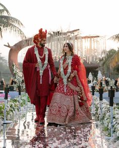 a man and woman dressed in red are walking down the aisle with flowers on it