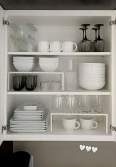 white dishes and cups are arranged on shelves in the kitchen, with hearts drawn on them