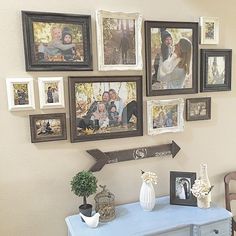 a bunch of pictures hanging on the wall next to a table with vases and flowers