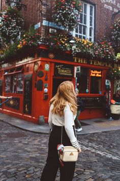 a woman is walking down the street with her purse in front of a red building