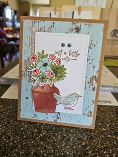 a close up of a card on a table with flowers in a pot and a bird