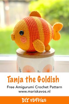 an orange crochet fish sitting on top of a white cup with the words tanja the goldfish