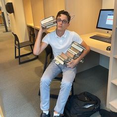 a man sitting in front of a desk with books on his lap, holding two stacks of books