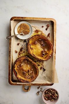 three baked desserts on a tray next to a bowl of nuts and a spoon