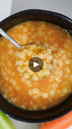 a bowl of soup with a spoon in it and carrots next to the bowl