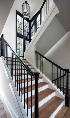 a white staircase with black handrails and wood flooring next to a large window