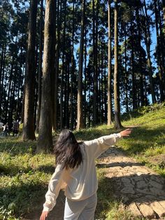 a woman walking down a path in the woods with her arms spread out to catch something