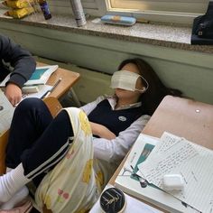 two people sitting at desks with masks on their faces