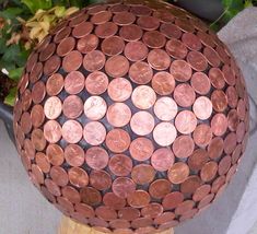 a sphere made out of pennets sitting on top of a wooden post next to a potted plant