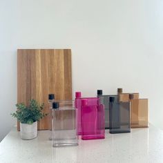 four different colored vases sitting next to each other on a white counter with a plant in the middle