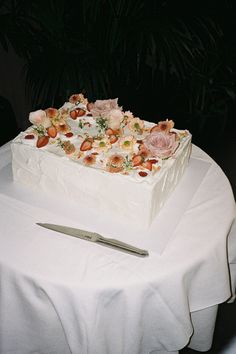 a square cake sitting on top of a table next to a knife and flower arrangement