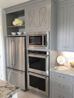 a kitchen with gray cabinets and stainless steel appliances in the center, along with marble counter tops