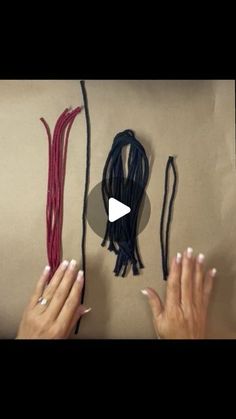 two hands are holding different colored cords and one is pointing at the string on the wall