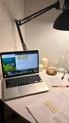 an open laptop computer sitting on top of a desk next to a lamp and papers